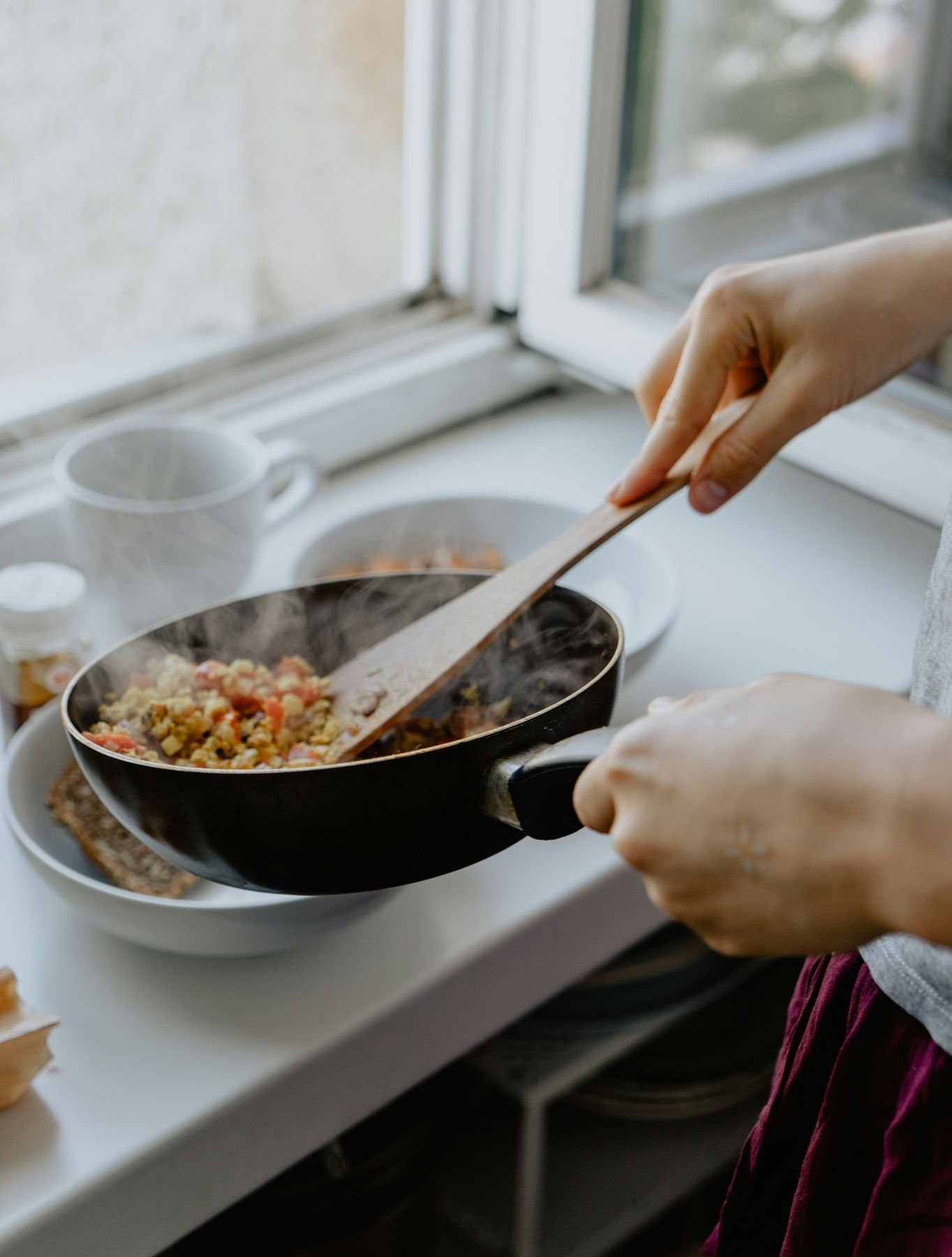 Cook stirring a pan of food by a kitchen window