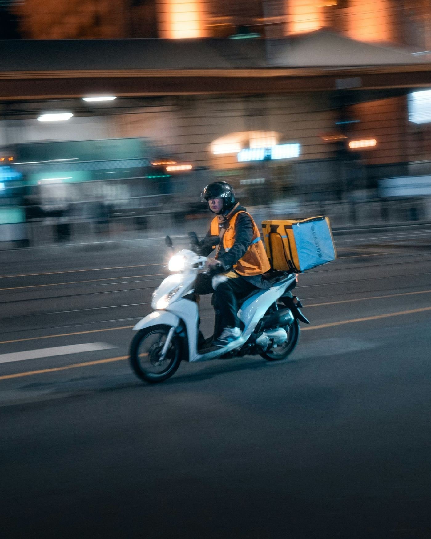 Delivery rider on a scooter carrying an insulated food box through the city at night