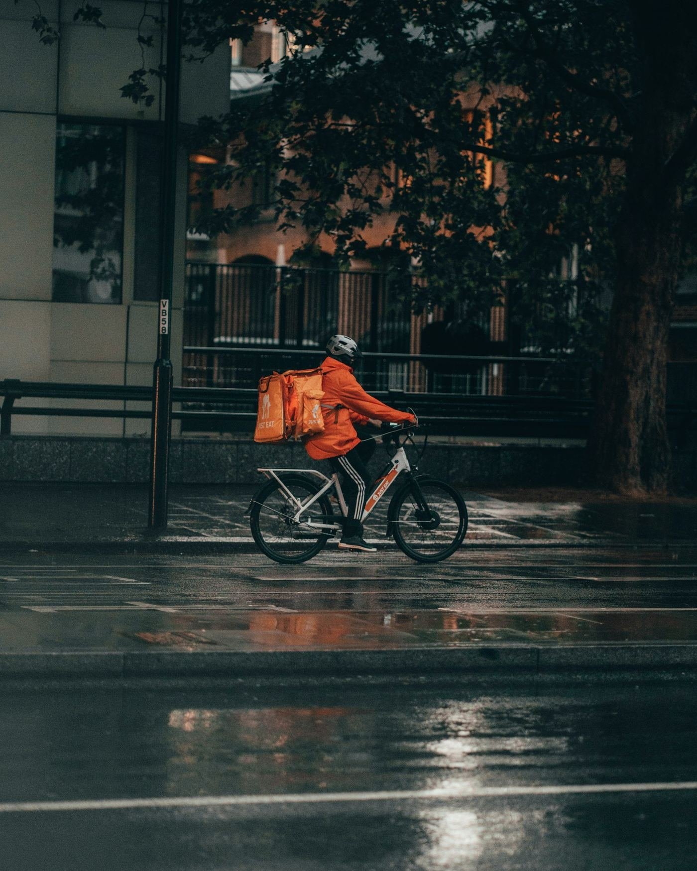 Delivery cyclist with an insulated food bag on a rainy city street at night