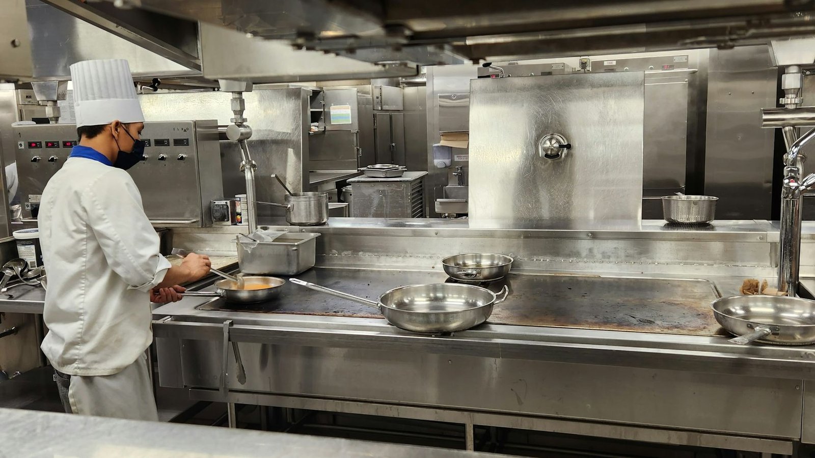 Chef cooking in a commercial delivery kitchen with stainless steel equipment and extraction
