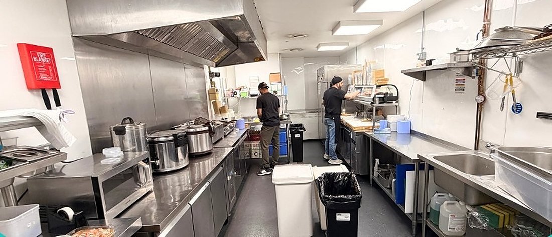 A larger Ready Kitchen production unit with long stainless steel counters and cooks preparing food