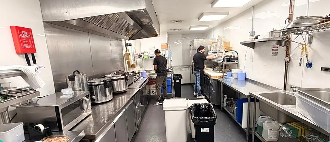A larger Ready Kitchen production unit with long stainless steel counters and cooks preparing food